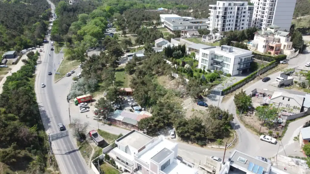 Tbilisi Real estate investment project: Lisi Lake Apartments site overview in Tbilisi. Drone view of investment land near Lisi Lake showing access roads, nearby residential buildings, and urban forest in Tbilisi – LD Estates