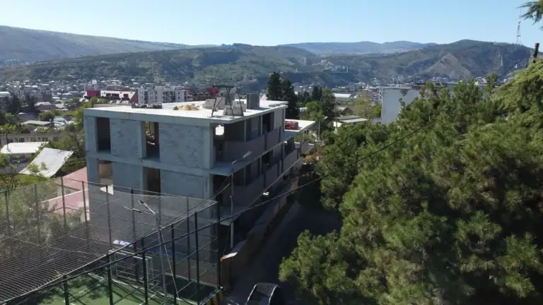 Real estate investment building in Tbilisi: Drone view of Avlabari real estate Real estate investment projects in Tbilisi - Avlabari office building under construction / LD Estates mid-rise building with city and mountain backdrop