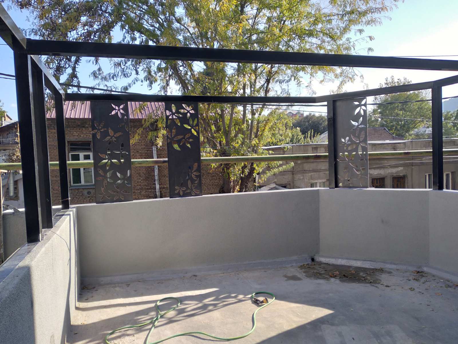 Second floor rooftop terrace with decorative laser-cut metal privacy panels featuring floral patterns, steel pergola frame, and views of neighboring historic buildings