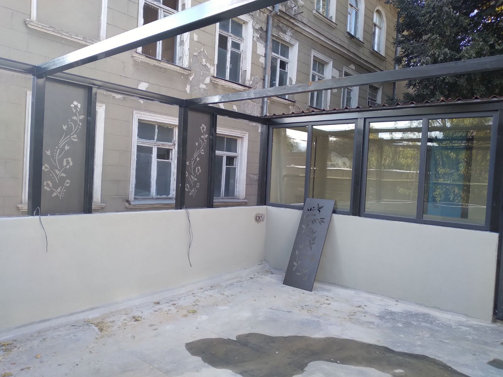 Rooftop terrace during final construction phase showing decorative metal panel installation, glass elements, and connection to adjacent heritage building