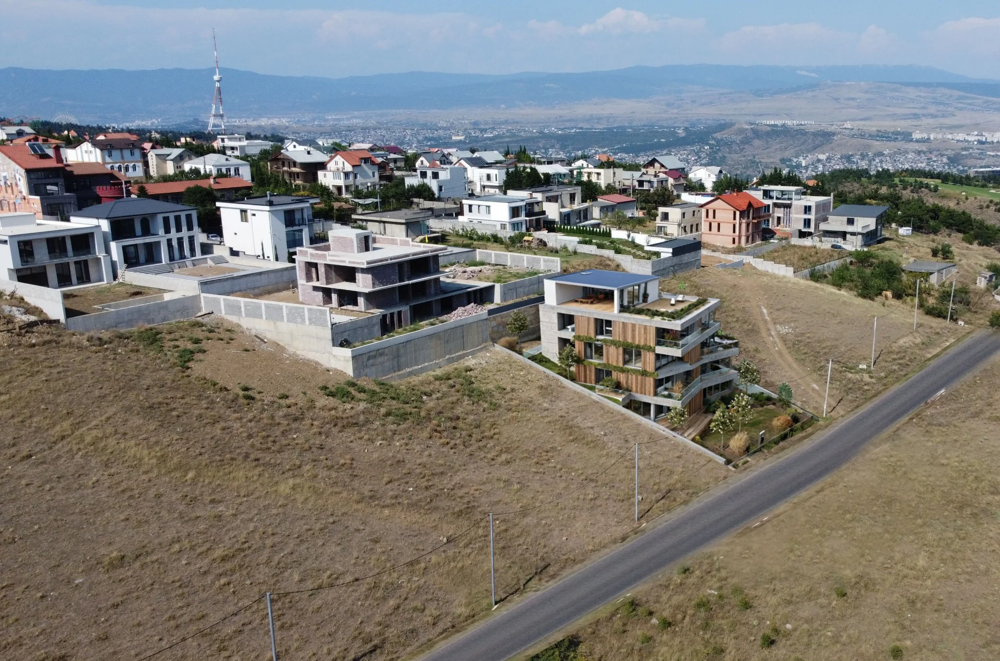 Aerial view of Tabor Hill residential neighborhood showing modern hillside villas, development activity, and Tbilisi TV tower in background with panoramic city views