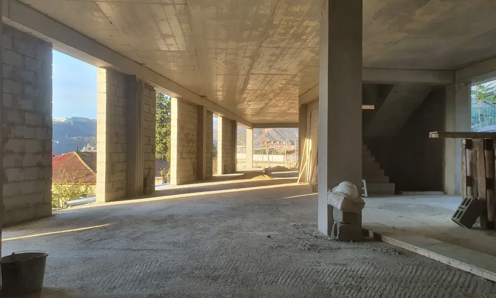 Interior photograph showing open floor plan with concrete columns, exposed ceiling slab, concrete block walls with large window openings